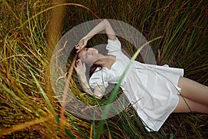 Romantic young woman in thick tall grass in field. Dreamy gentle woman in a white dress in nature. Natural beauty, enjoyment of