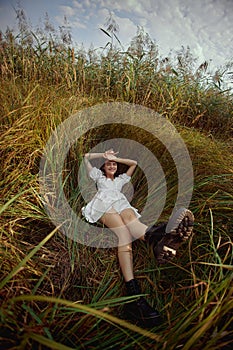 Romantic young woman in thick tall grass in field. Dreamy gentle woman in a white dress in nature. Natural beauty, enjoyment of