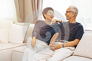 RomantiRomantic senior Asian couple laughing and sitting on sofa at home.