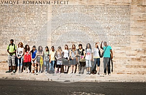 Group of diverse 20's turned in street under wall covered with roman text outside Ara Pacis in Rome