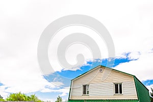 Roof of the attic with two windows in the house against the blue sky with clouds