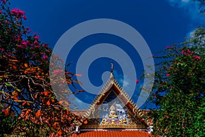 The roof of a Buddhist temple with the image of the Buddha and blooming trees against the blue sky. Buddhist temples in