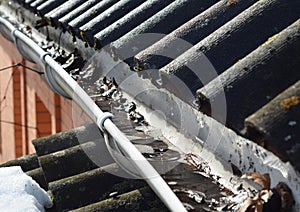 Roof gutter cleaning. A clogged rain gutter of an asbestos roof with non flowing water from melted snow because of unclean gutters