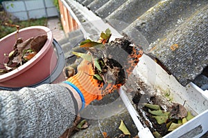 Roof Gutter Cleaning from Leaves in Autumn with hand. Roof Gutter Cleaning Tips. photo