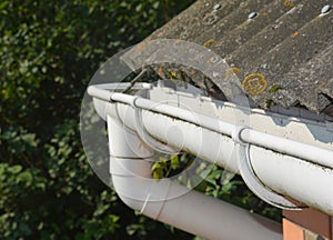 Roof gutter. House asbestos roof with plastic roof gutter pipe. House guttering with holders and old asbestos roof