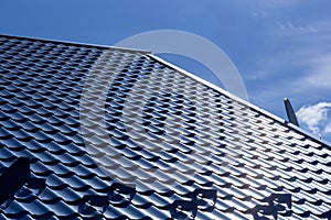 The roof of a house covered with sheets of blue metal tiles against the background of the sky on a summer day. Business selling