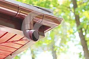 Roof of house with plastic rain gutter on beautiful natural background with green vegetation