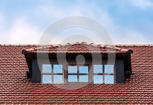 The roof of the house is tiled. Window on the roof of the house. Attic. Blue cloudy sky