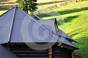 The roof is made of gray embossed metal sheets. Wooden house in the summer fiel