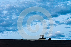 Roof with metal chimney and evening sky with clouds blue hour