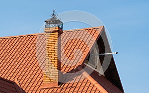 Roof of a new home. Ceramic chimney, orange metal roof tiles. TV antenna. A modern house against a blue sky