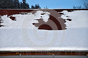 Roof with rain gutter in winter. Roof with asphalt shingles covered with snow and icicles