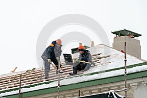 Roof repairs in winter. Two workers repair the roof on a frosty and snowy day. Men with shovels remove snow from the roof