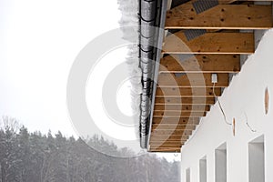 The roof of a single-family house is covered with snow, visible roof trusses and a hanging cap of snow on the gutter.