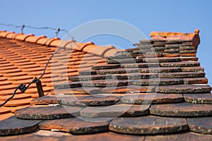 The roof of a tall house on which there are slates and a wire lightning rod