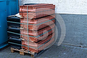 Roof tiles in black and brown-terracotta stacked on a palett.