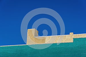 Roof tops seen against a blue sky in Cody, Wyoming, show bright colors of yellow & green stucco & painted cement blocks. Clean str