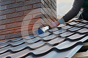 Roofer builder worker attach metal sheet to the chimney. Unfinished roof construction