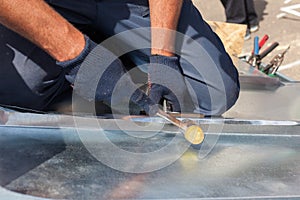 Roofer builder worker finishing folding a metal sheet using rubber mallet.