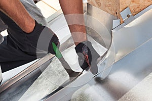 Roofer builder worker finishing folding a metal sheet using special pliers with a large flat grip.