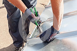 Roofer builder worker finishing folding a metal sheet using special pliers with a large flat grip.