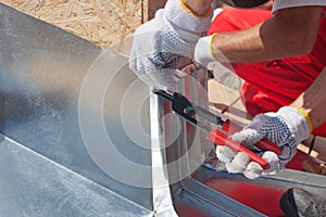 Roofer builder worker finishing folding a metal sheet using special pliers with a large flat grip.