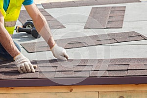 Roofer builder worker installing Asphalt Shingles or Bitumen Tiles on a new house under construction.