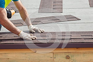 Roofer builder worker installing Asphalt Shingles or Bitumen Tiles on a new house under construction