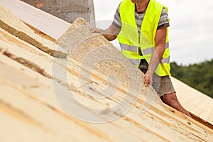 Roofer builder worker installing roof insulation material on new house under construction.