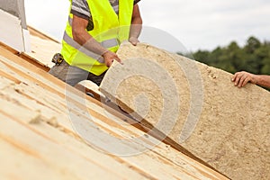 Roofer builder worker installing roof insulation material on new house under construction.