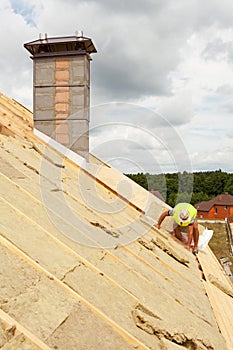 Roofer builder worker installing roof insulation material rockwool on new house under construction.