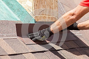 Roofer builder worker installing shingles on a new wooden roof with skylight.