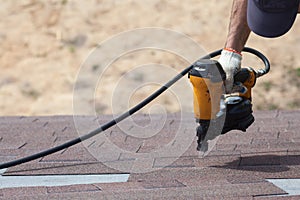Roofer builder worker with nailgun installing Asphalt Shingles or Bitumen Tiles on a new house under construction.