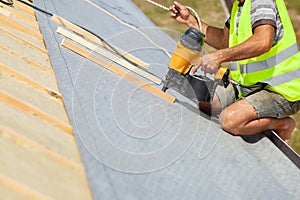 Roofer builder worker use automatic nailgun to attach roofing membrane. photo