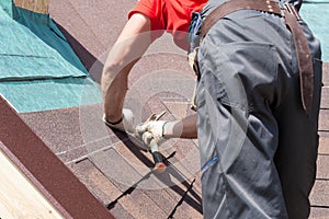 Roofer builder worker use a hammer for installing roofing shingles.