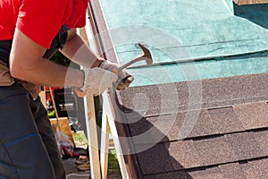 Roofer builder worker use a hammer for installing roofing shingles.