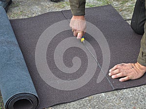 Roofer cutting roll roofing felt or bitumen during waterproofing works.