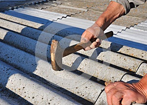 Roofer hammering nail in asbestos old roof tiles. Roofing construction