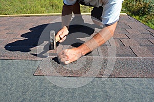 Roofer installing Asphalt Shingles on house Roofing Construction with hammer and nails in motion