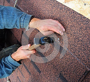 Roofer installs bitumen roof shingles - closeup on hands. Roofing repair photo