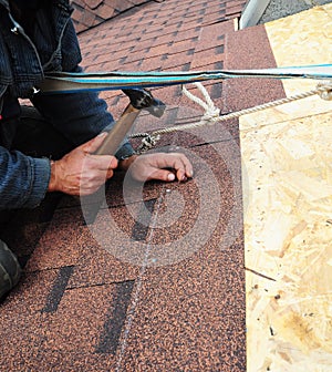 Roofer installs bitumen roof shingles with hammer and nails. Roofing photo