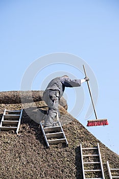 Roofer with ladders on a thatched roof to remove moss and dirt w