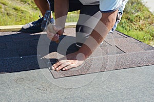 Roofer repair, renovating, installing asphalt shingles on house roofing construction with hammer and nails in action.  Roof repair