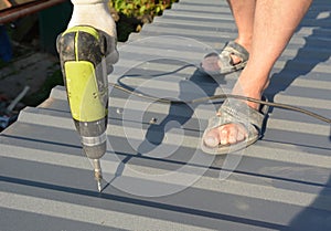 Roofer with screw gun installing  lightweight metal roof tiles roofing  construction