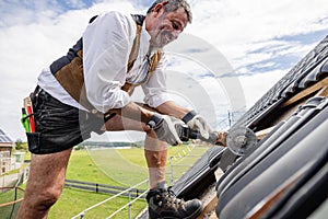 Roofer in traditional gear working on roof using saw