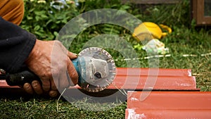 Roofer using an angle grinder machine to cut a roof tile of red color. Stock footage. Close up of male worker hands
