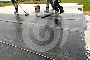 Roofer worker painting bitumen praimer at concrete surface by the roller brush Waterproofing