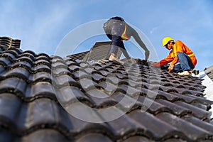 2 roofers working on the working at height to install the Concrete Roof Tiles on the new roof of new modern building construction