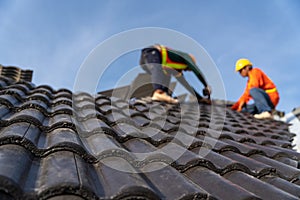 2 roofers working on the working at height to install the Concrete Roof Tiles on the new roof of new modern building construction