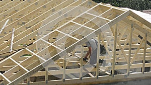 A roofing carpenter works to install the roof of an unfinished house.